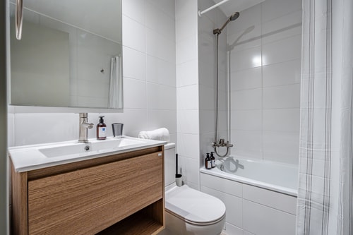 Baño con tina, ducha, inodoro y lavamanos sobre mueble de madera, con toallas dispuestas.