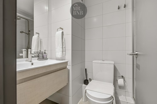 Baño con mueble de madera clara, lavamanos, toallas blancas e inodoro