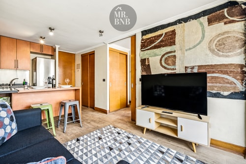 Living con sofá, taburetes, mueble bajo de TV, tapiz decorativo y alfombra geométrica