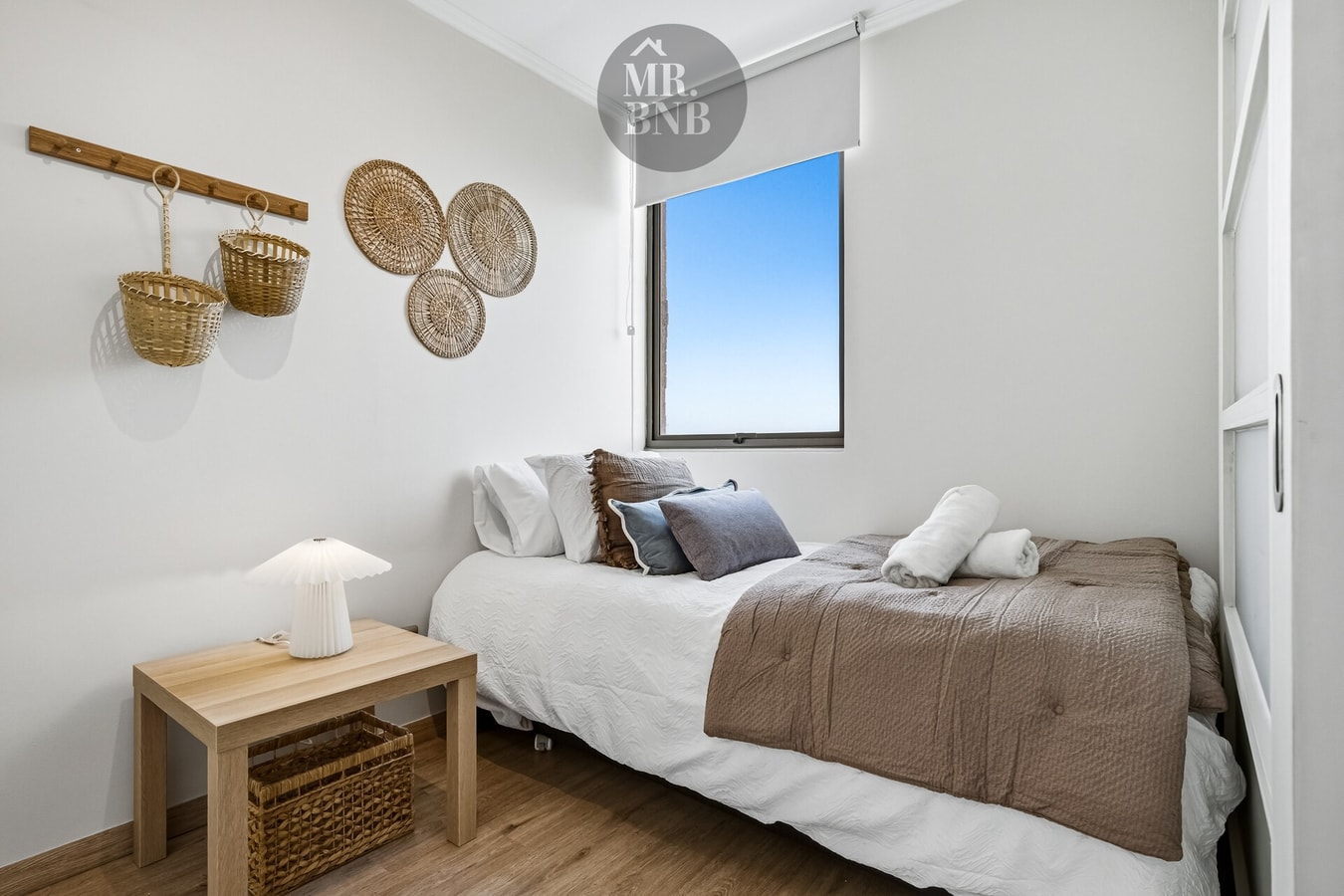 Dormitorio con cama de dos plazas, cojines y decoración de cestas en la pared