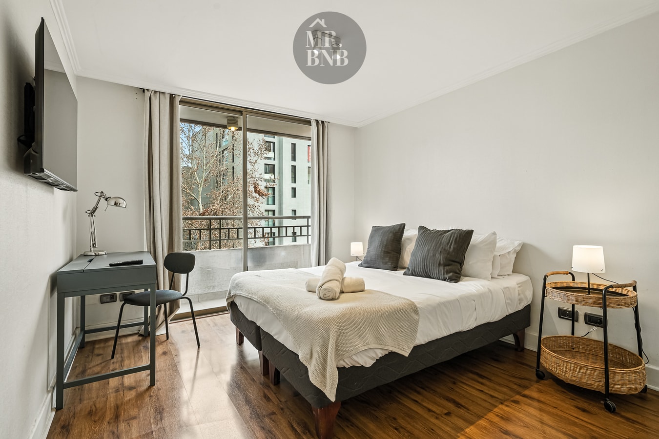 Dormitorio con cama matrimonial, televisor, escritorio con silla y ventanal con vista a la ciudad