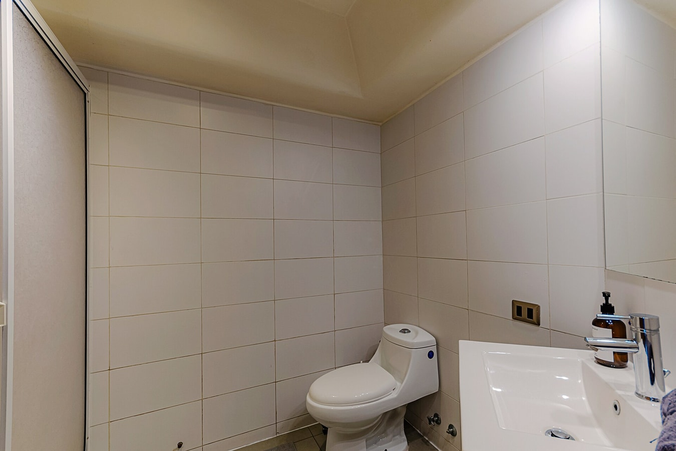 Baño con inodoro, lavamanos y mueble de guardado, revestido en cerámica clara.