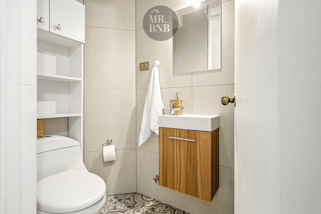 Baño con lavamanos sobre mueble de madera, inodoro y repisas