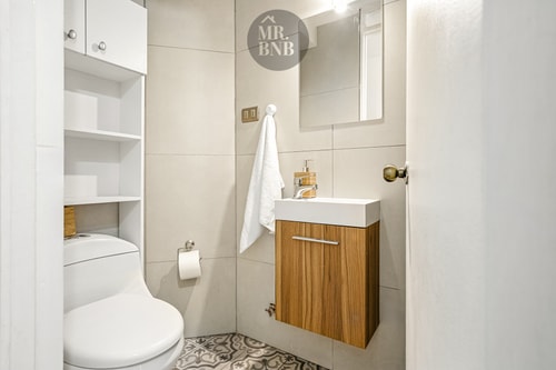 Baño con lavamanos sobre mueble de madera, inodoro y repisas