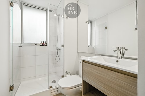 Baño con ducha de vidrio, tina, lavamanos con mueble de madera e inodoro