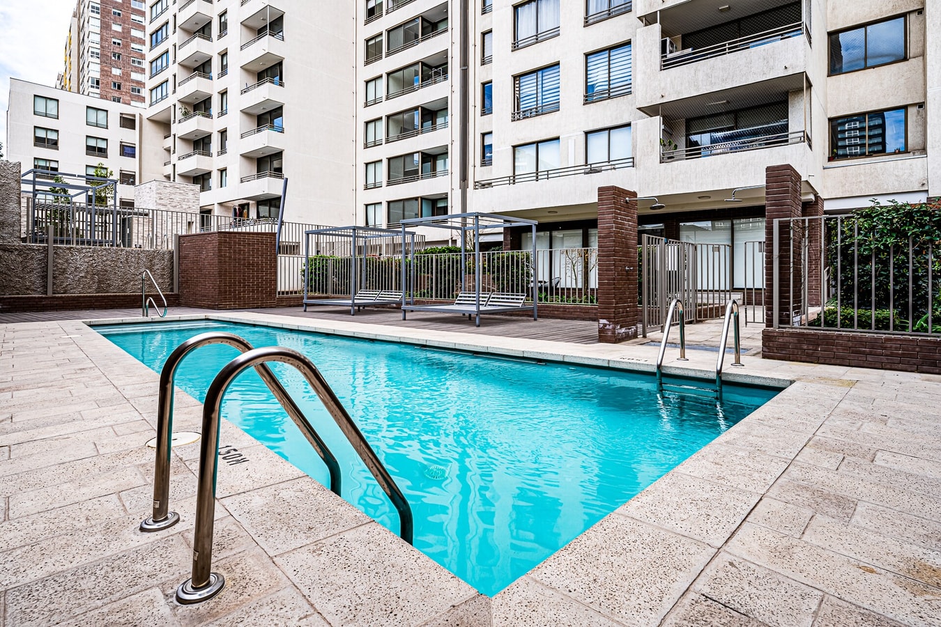 Piscina del edificio, rodeada de terraza y con vista a otros edificios