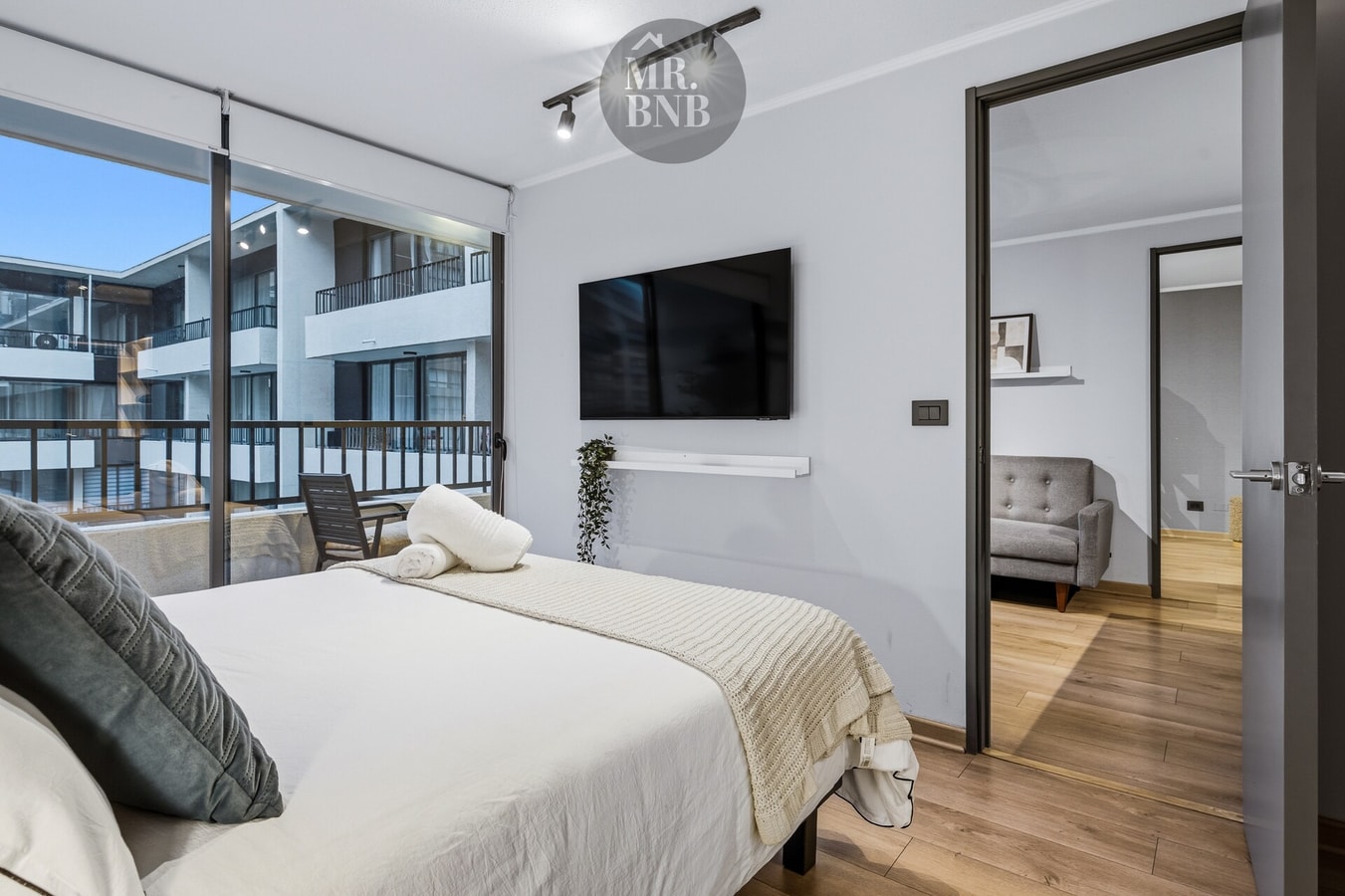 Dormitorio con cama, TV montada en la pared y ventanal con vista a edificios