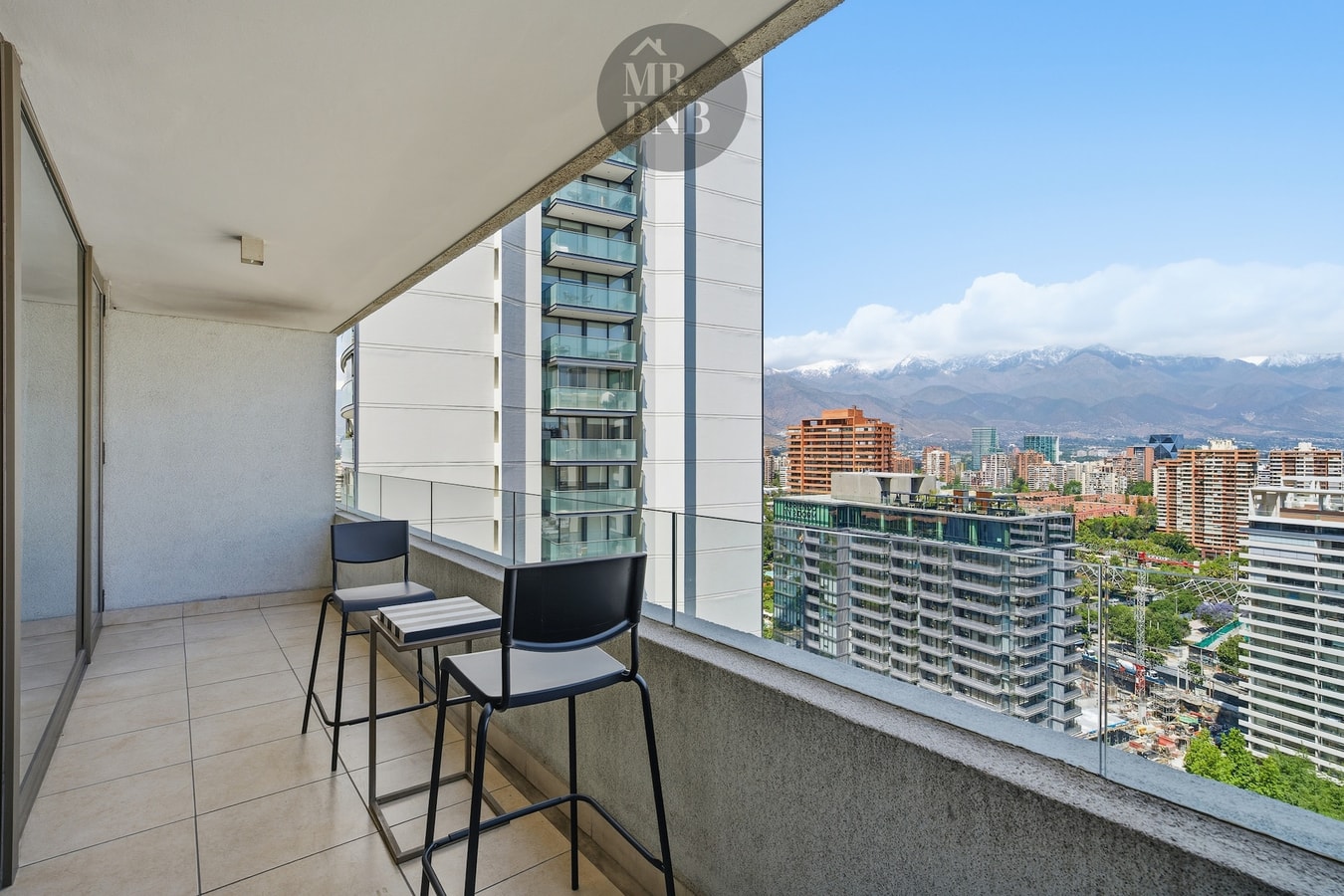 Terraza con dos sillas altas, baranda de vidrio y vista panorámica a la cordillera