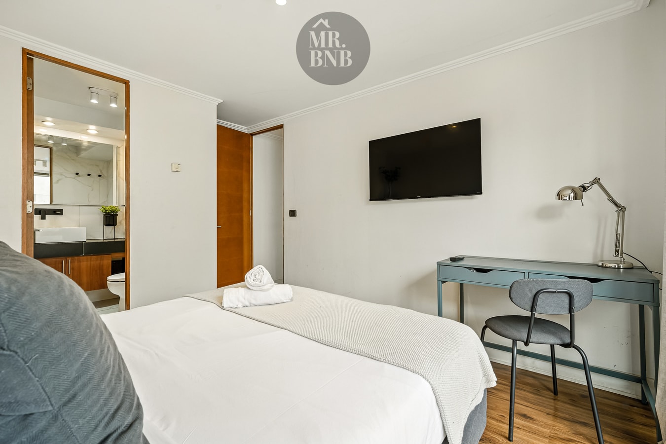 Dormitorio con cama, espejo de cuerpo entero, televisor y escritorio con silla