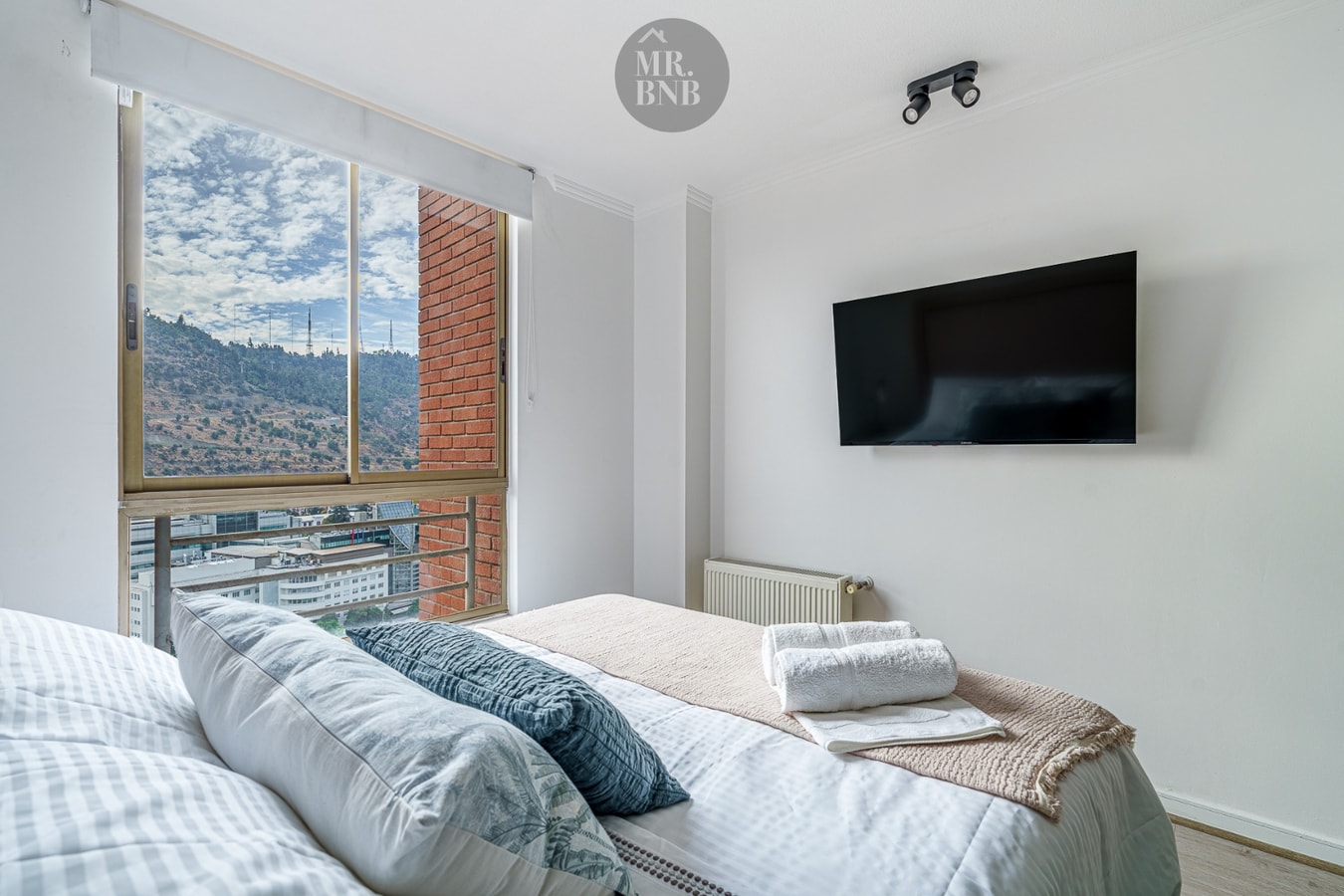 Dormitorio con cama matrimonial, televisor de pantalla plana y ventanal con vista urbana