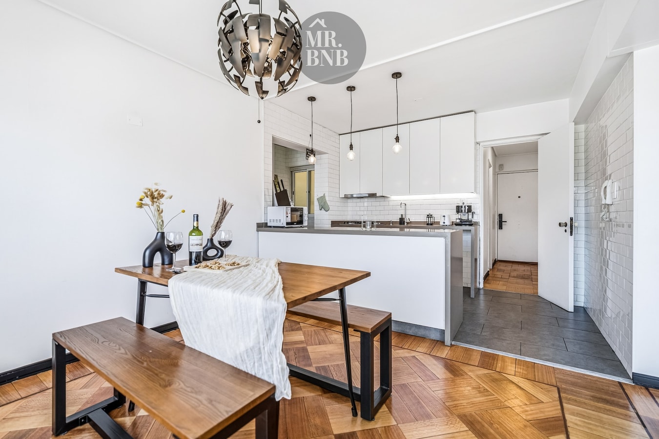 Comedor con mesa de madera, banca, lámpara colgante y acceso a la cocina