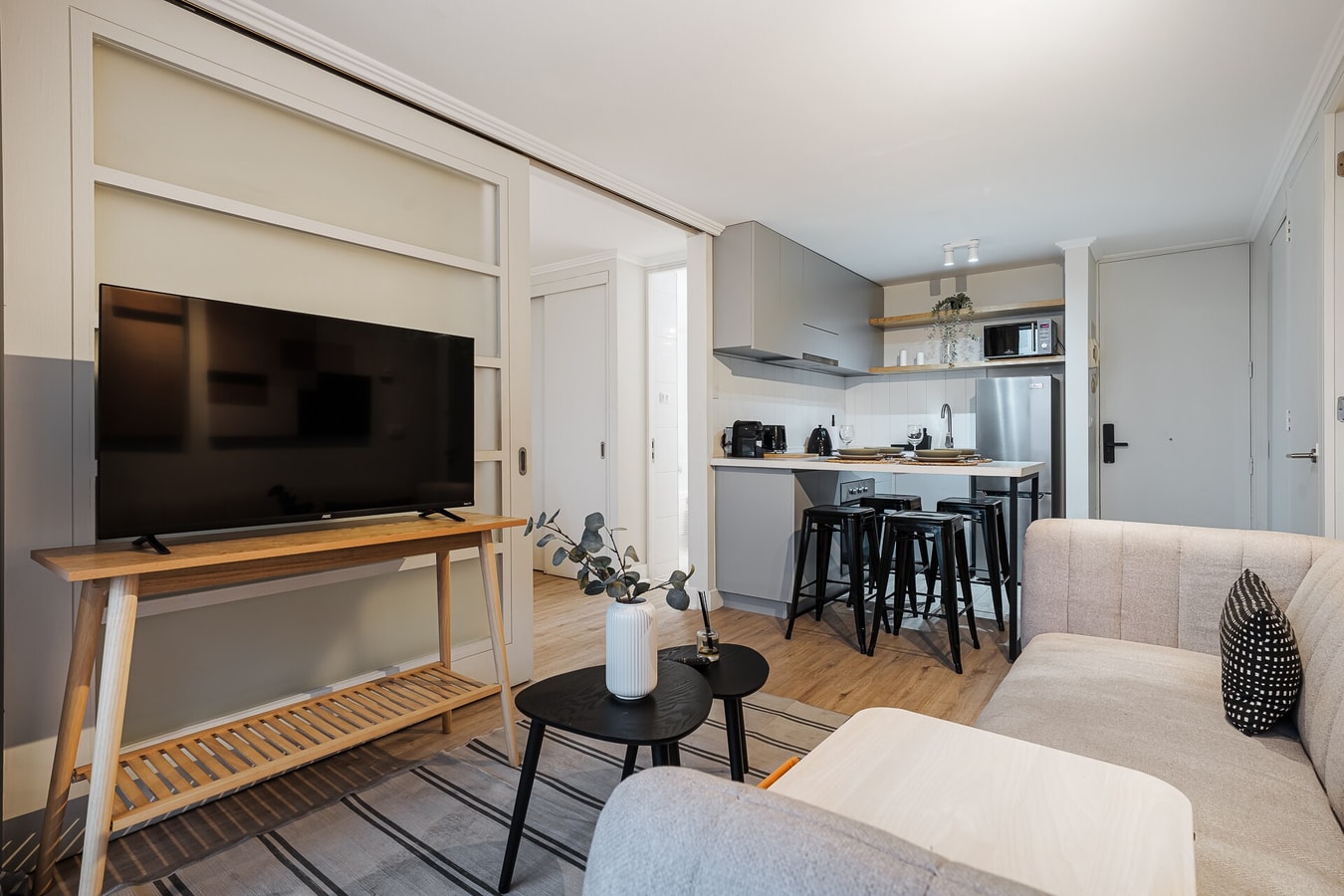 Living con TV sobre mueble, sofá y cocina con barra al fondo