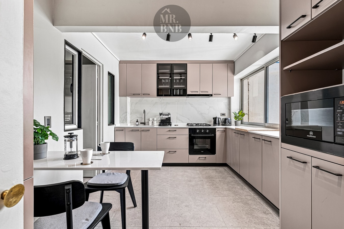 Cocina con muebles color rosado, mesa de comedor con sillas y ventanales