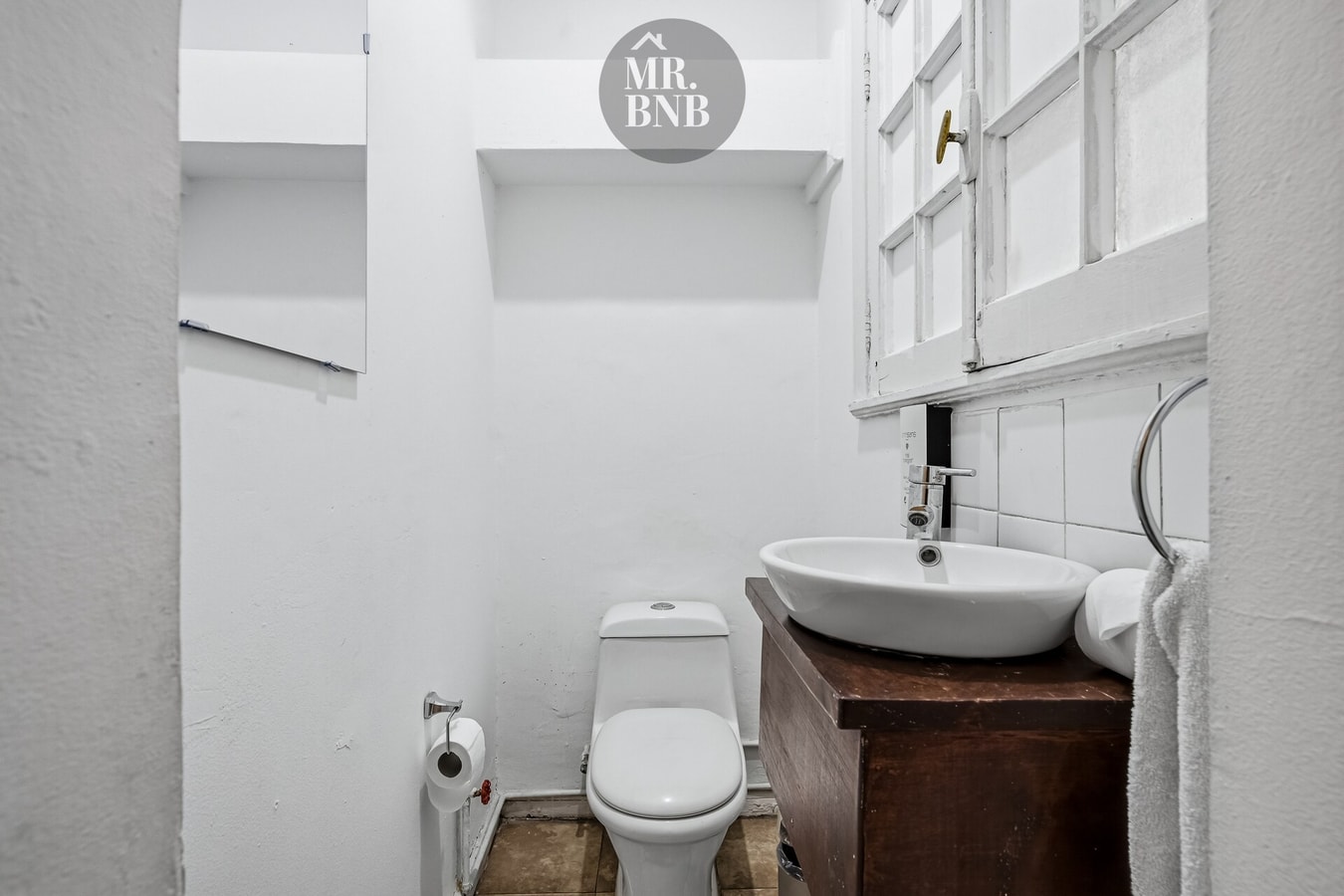 Baño con lavamanos sobre mueble de madera, inodoro y ventana con luz natural.