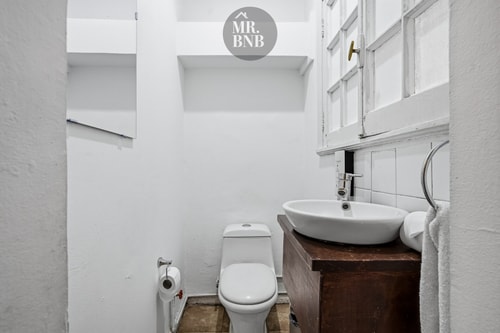 Baño con lavamanos sobre mueble de madera, inodoro y ventana con luz natural.