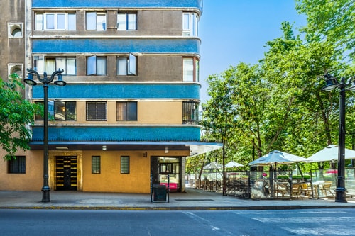 Fachada del edificio y calle con árboles y toldos de locales