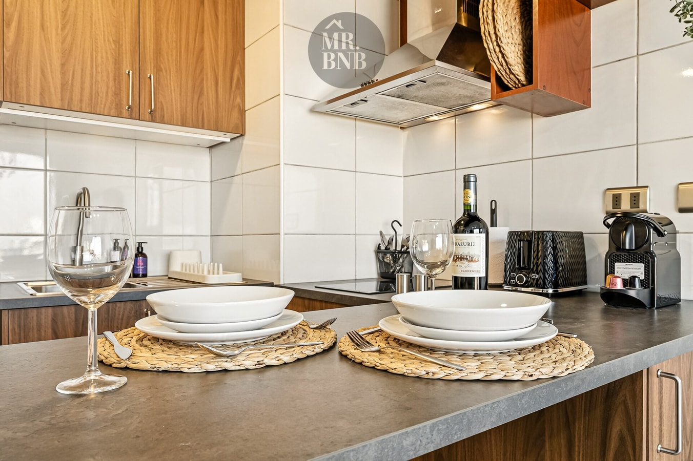 Detalle de barra de cocina con vajilla dispuesta, copas de vino y máquina de café