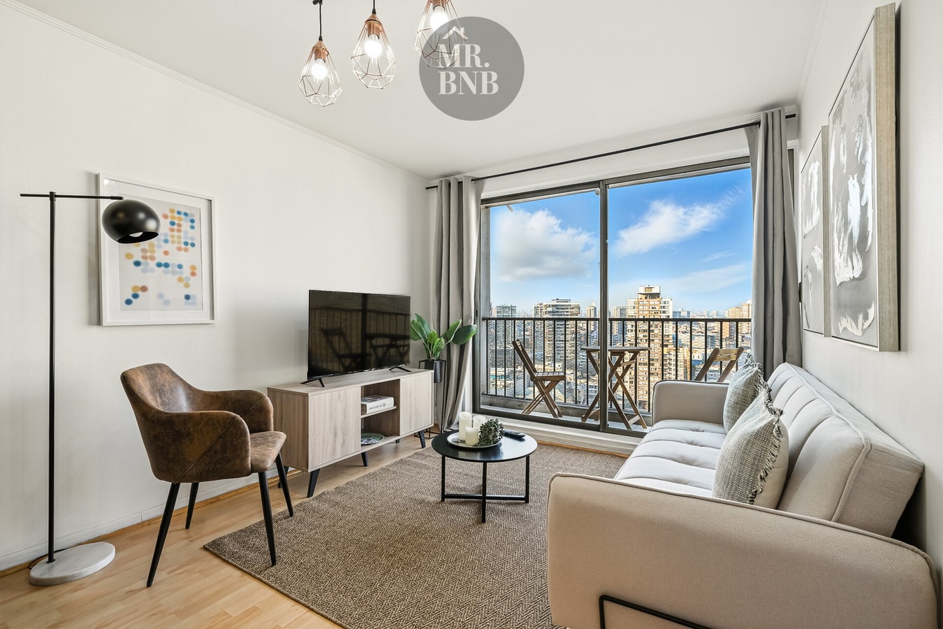 Living con sofá gris, sillón de cuero, mesa de centro y ventanal con vista a la ciudad