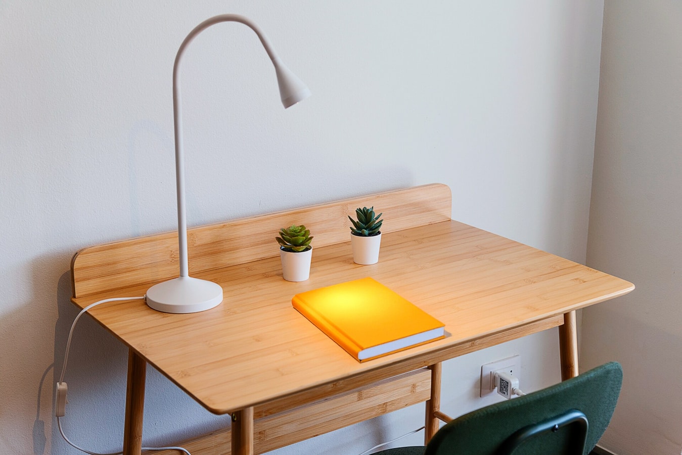 Escritorio de madera con lámpara flexible, dos suculentas y silla, apoyado contra la pared del dormitorio
