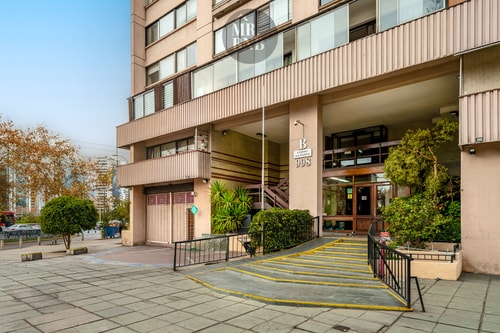 Acceso y fachada del edificio con jardineras y estacionamientos techados en la entrada.