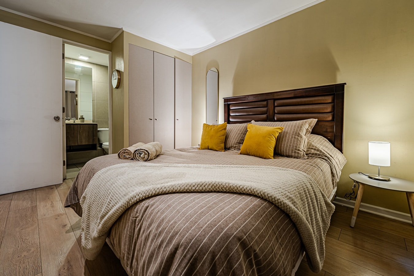 Dormitorio con cama matrimonial, cojines mostaza y velador
