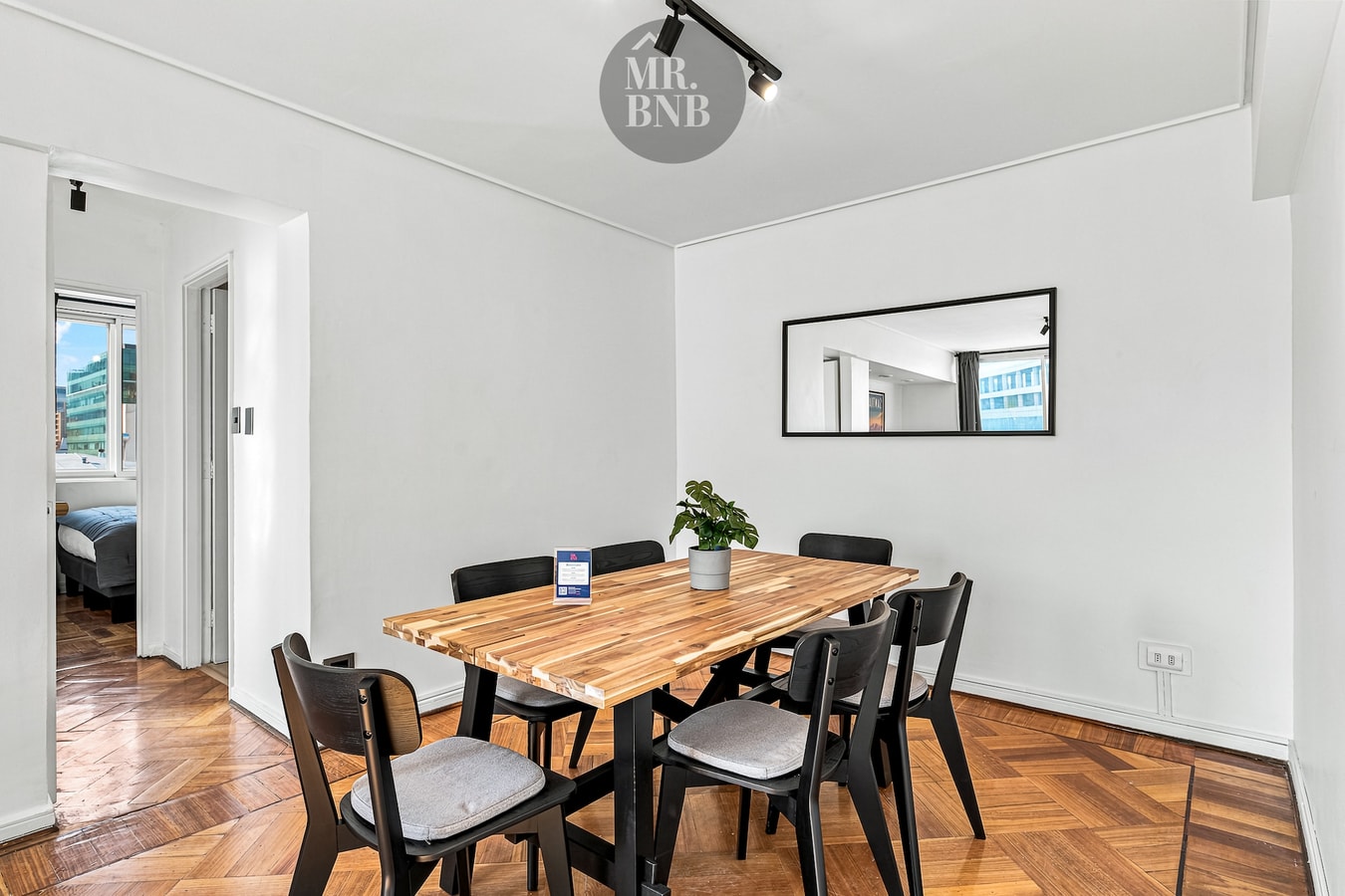 Comedor con mesa de madera, sillas negras y gris, y espejo en la pared