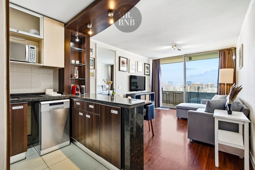 Cocina con microondas, lavaplatos y living al fondo con ventanal