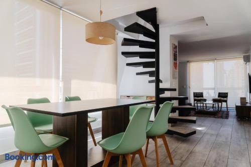 Comedor con mesa y sillas verdes junto a escalera caracol, con ventanal amplio y vista a edificios
