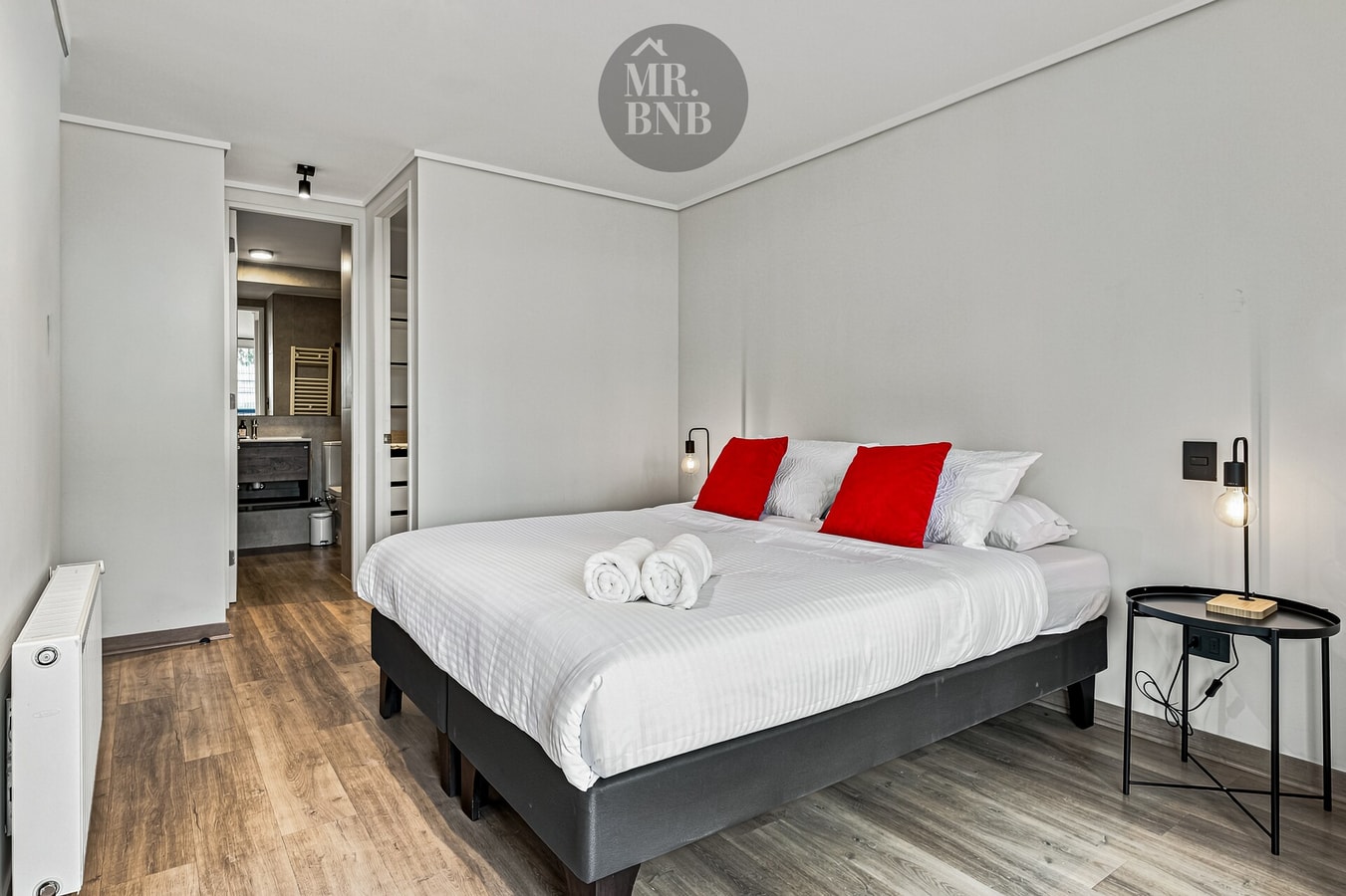 Dormitorio con cama de dos plazas, cojines rojos, veladores y radiador.