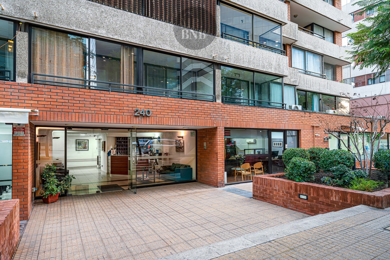 Fachada y acceso del edificio, hall vidriado con mobiliario y jardineras