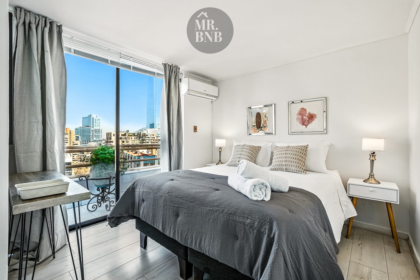 Dormitorio con cama, veladores, escritorio y ventanal con aire acondicionado