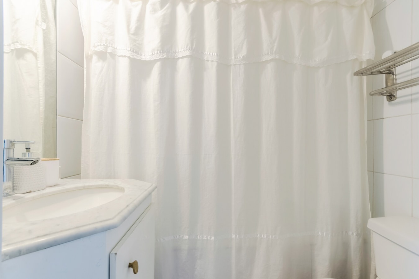 Baño con cortina de baño blanca, lavamanos y mueble bajo