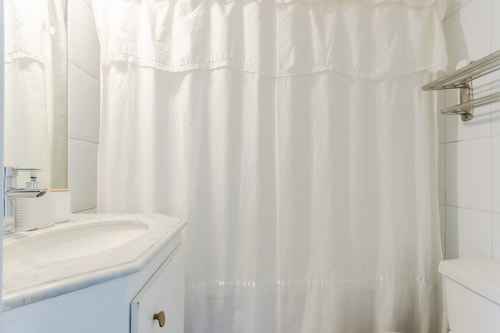 Baño con cortina de baño blanca, lavamanos y mueble bajo