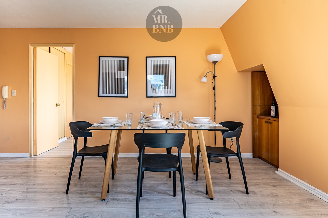 Comedor con mesa de madera, seis sillas negras y cuadros en la pared