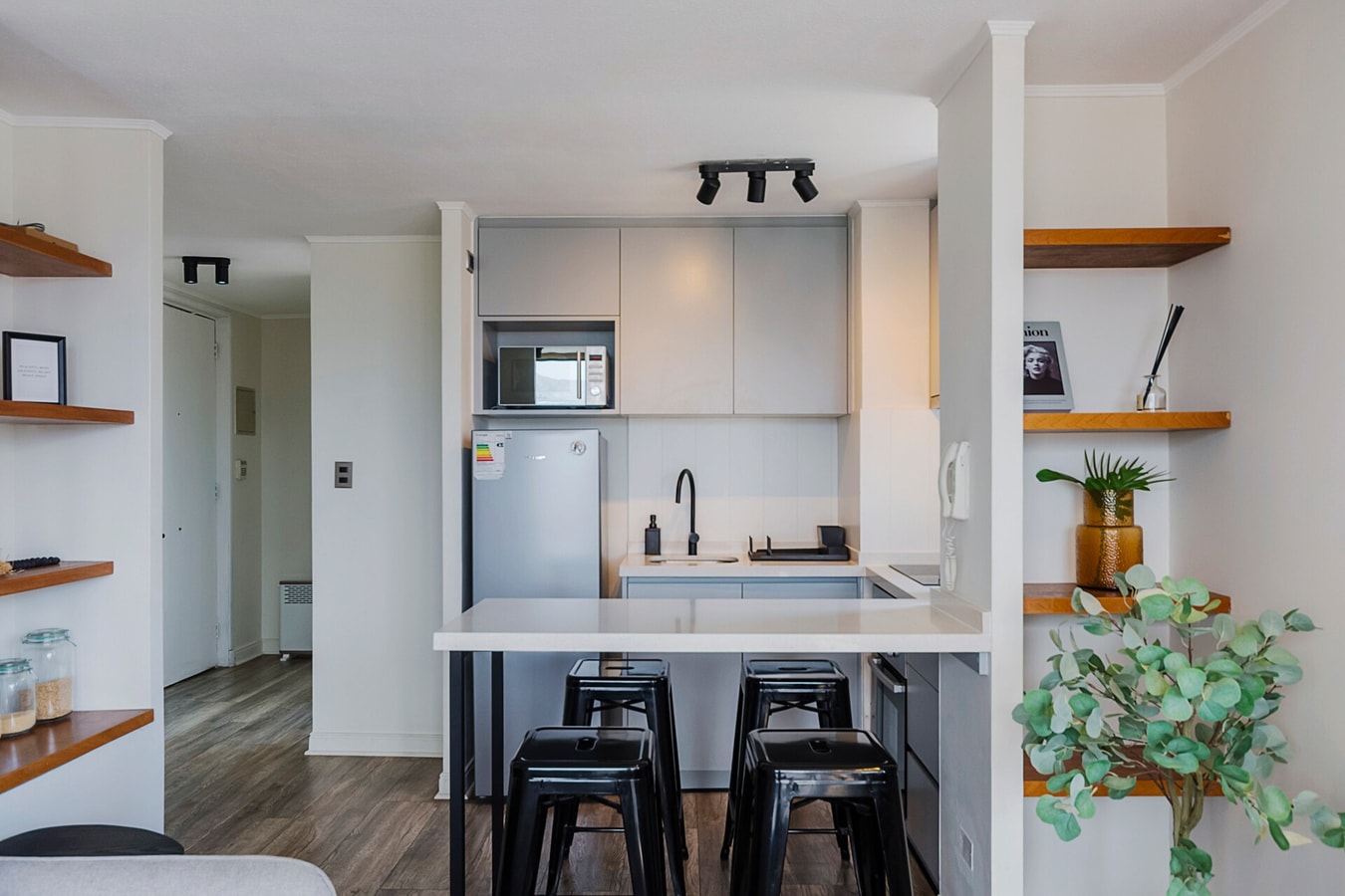 Cocina con barra, taburetes, repisas de madera y refrigerador