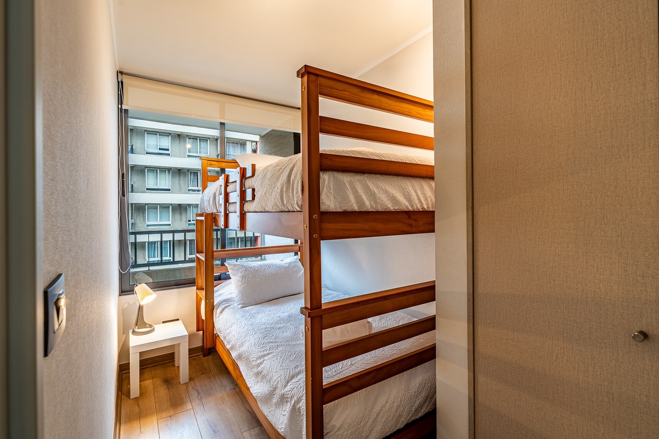 Dormitorio con litera de madera y ventana con vista a edificios.