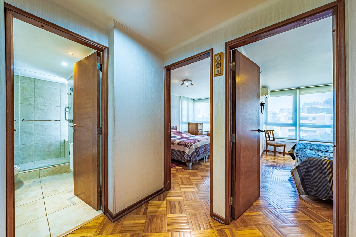 Pasillo con puertas abiertas hacia el baño y un dormitorio, piso de parqué en toda la circulación.