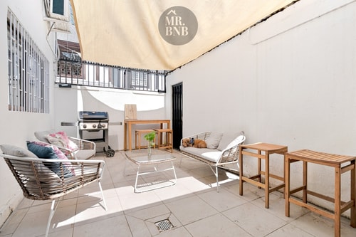 Patio privado con toldo, parrilla a gas Weber, sillones exteriores y mesa de centro, con piso de cerámica.