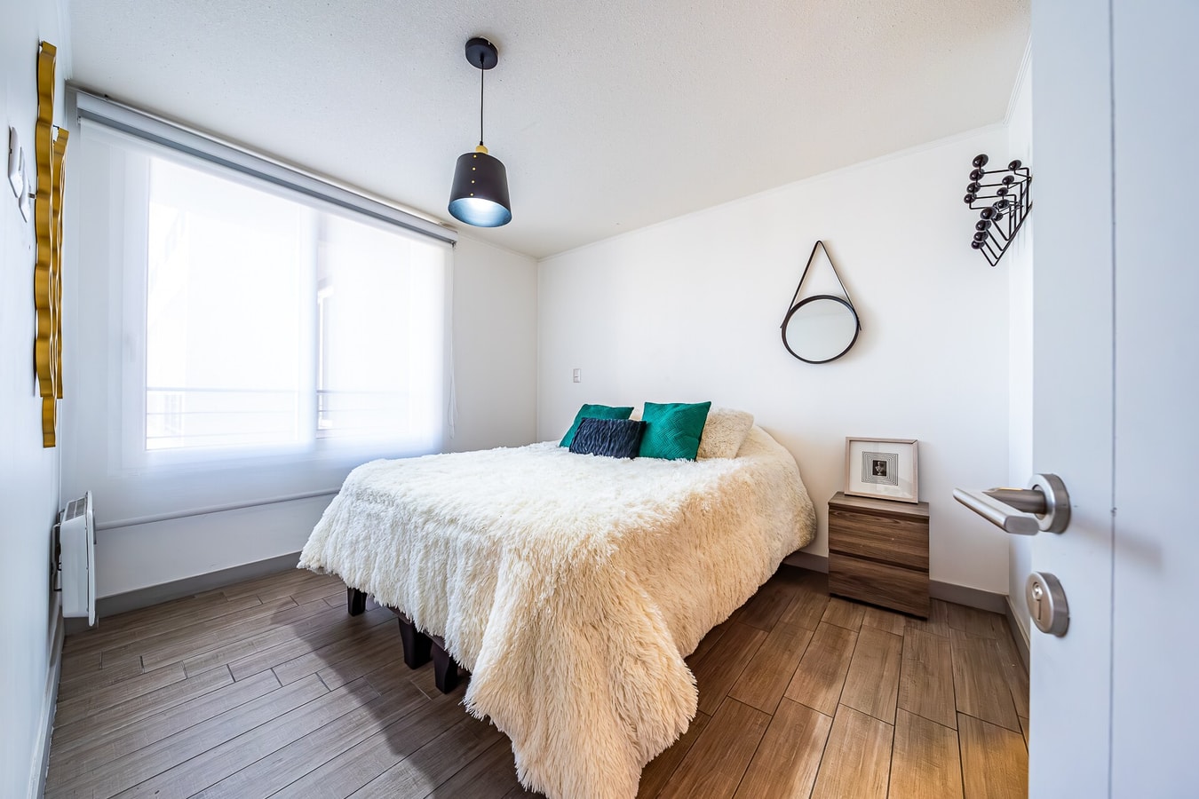 Dormitorio con cama de dos plazas, ropa de cama color crudo, velador de madera y ventana con cortina