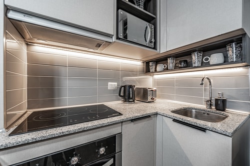 Cocina en L equipada con encimera de vitrocerámica, campana, mesón de piedra clara y utensilios