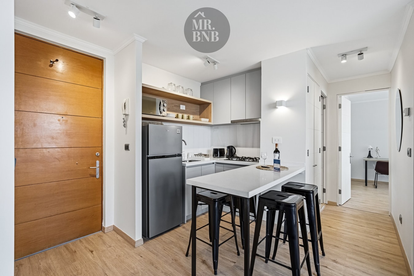Hall de acceso al departamento con puerta de madera y cocina con refrigerador al fondo