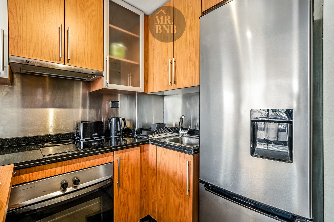 Cocina con muebles de madera, refrigerador, campana, horno y encimera