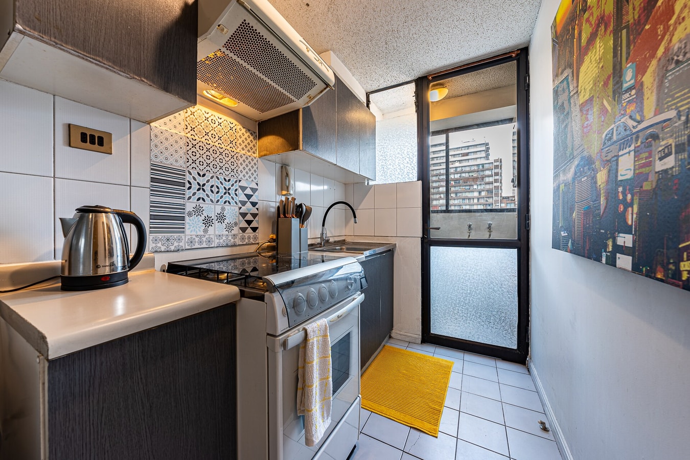 Cocina equipada con campana extractora, encimera, hervidor eléctrico y puerta corredera hacia el balcón.