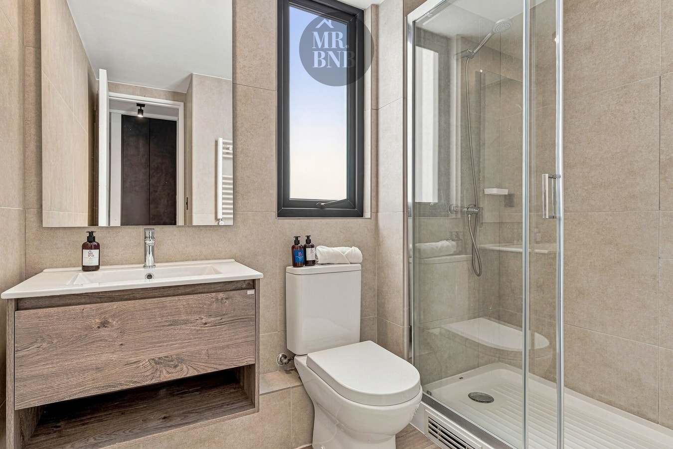 Baño con ducha de vidrio, mueble vanitorio de madera y ventana