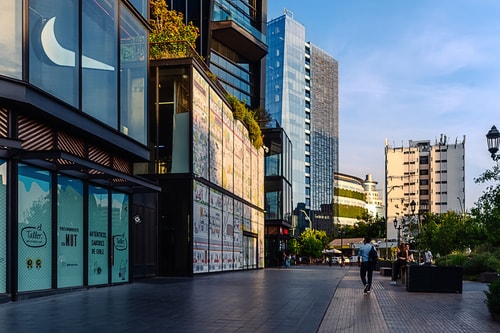 Calle comercial frente al edificio con locales y transeúntes.