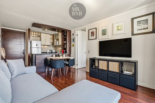 Living con sofá, mueble bajo televisor y comedor junto a la cocina
