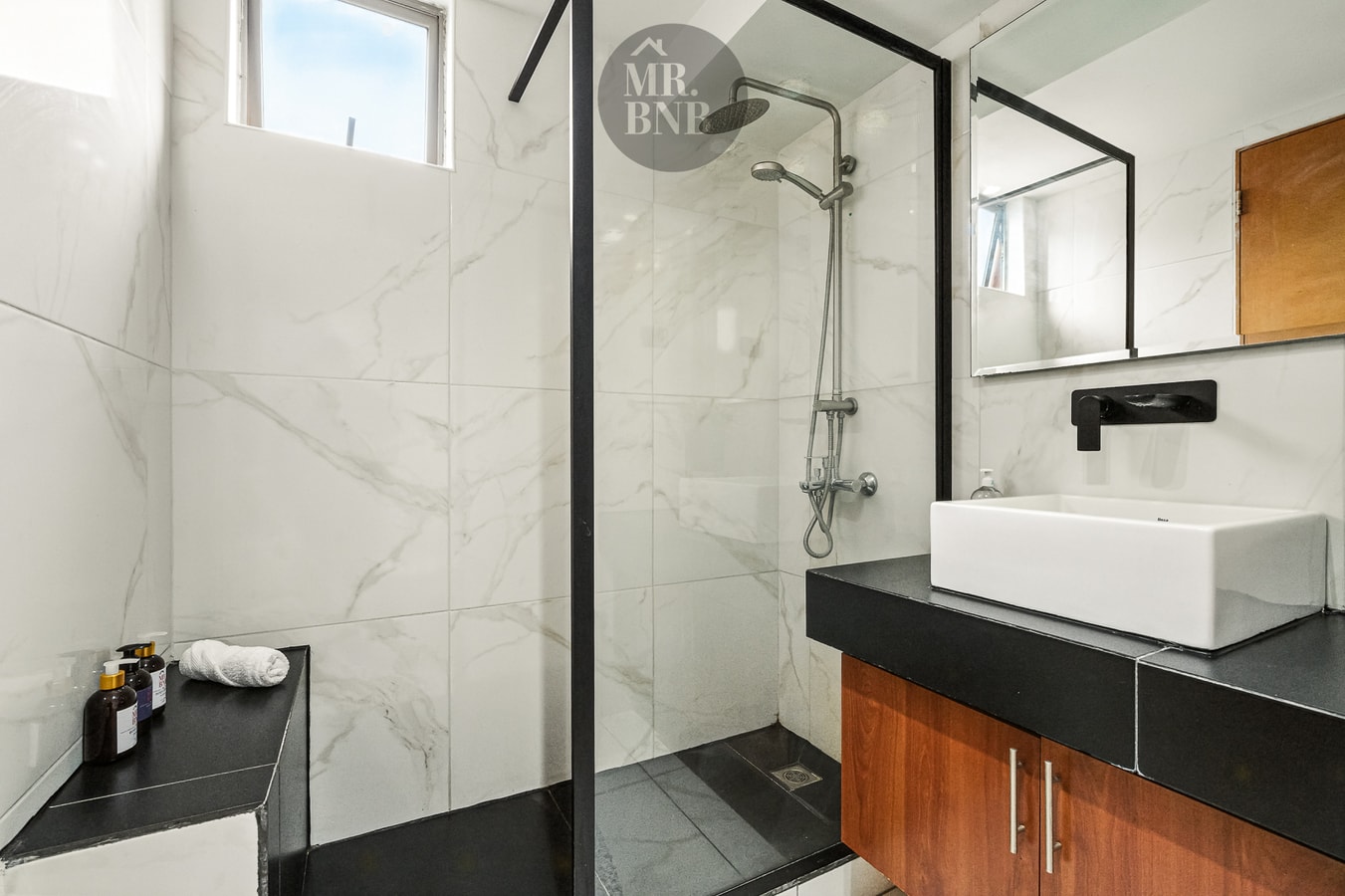 Baño con ducha de mampara de vidrio, revestimiento en cerámica blanca y ventana