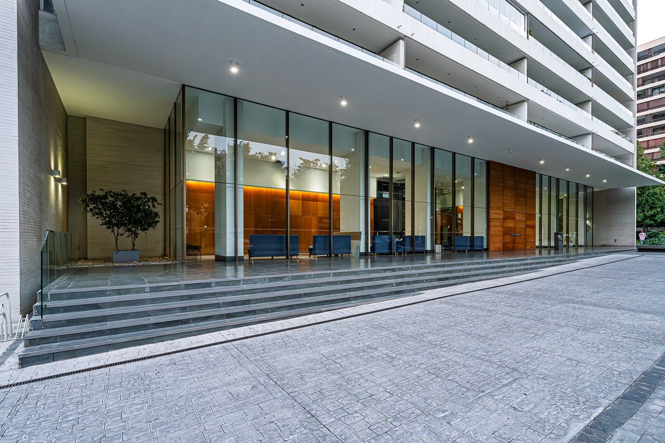 Fachada de acceso del edificio con hall vidriado y jardinera exterior.