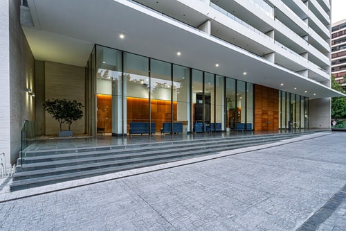 Fachada de acceso del edificio con hall vidriado y jardinera exterior.