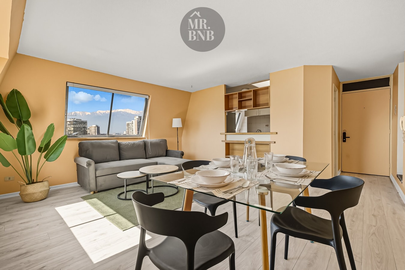 Living comedor con sofá gris, mesa de vidrio con vajilla y planta ornamental